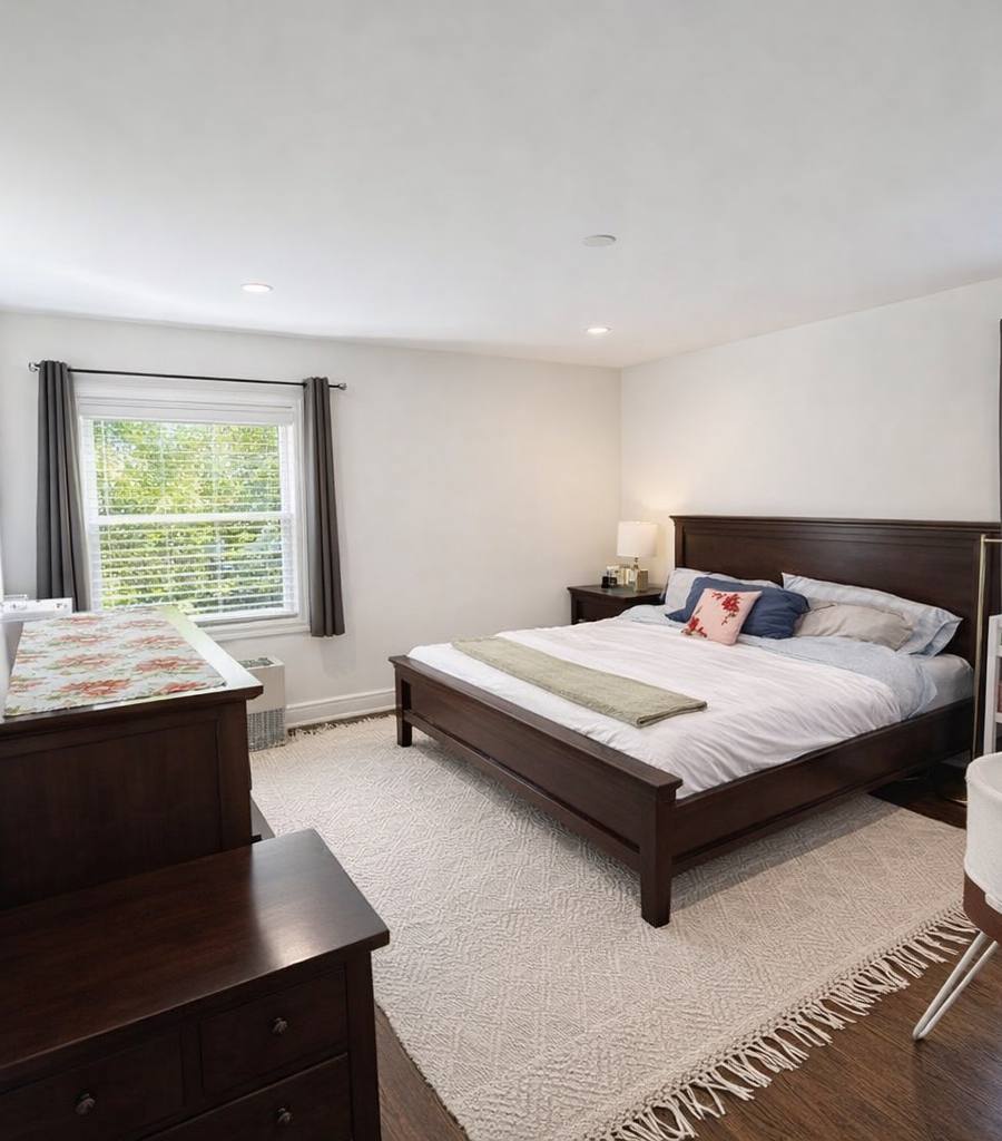 Warm, bright master bedroom with dark walnut furniture, a bassinet and crib, and two daylit windows after photo enhancement